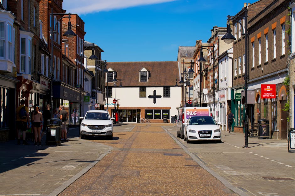 A narrow residential street with a gently curving tarmac road lined by brick terraced houses featuring bay windows, chimneys, and pitched roofs, set against a backdrop of leafless trees and overcast s