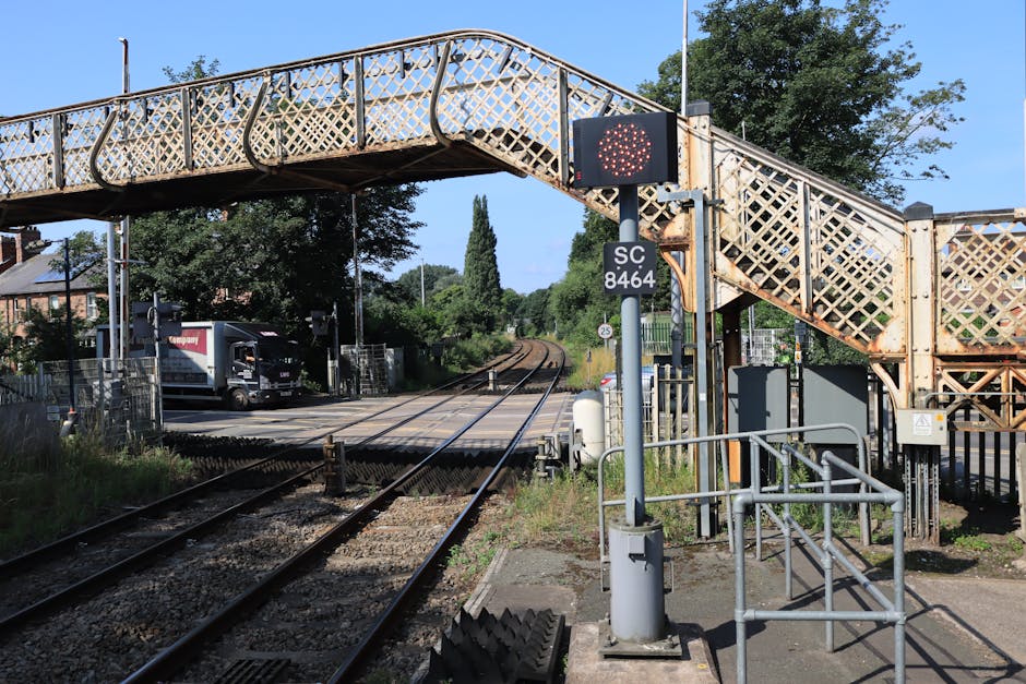 A clear view from Enfield Town train station platform showing train tracks extending into the distance, bordered by a concrete edge on one side and a small shelter with a white roof on the other. The 