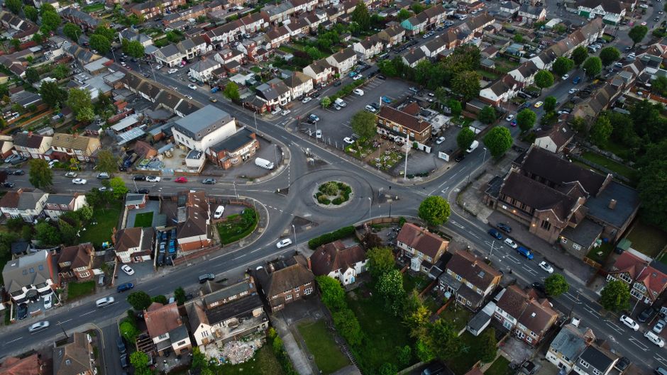 An aerial view of a residential neighbourhood in Enfield Town showing a busy roundabout with a central traffic island landscaped with greenery and small trees. Surrounding the roundabout are roads wit